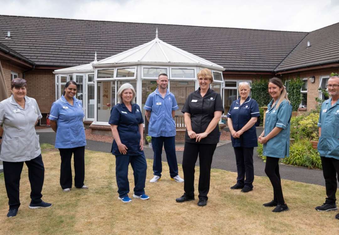 8 staff members stand outside the care homes conservatory surrounded by garden space