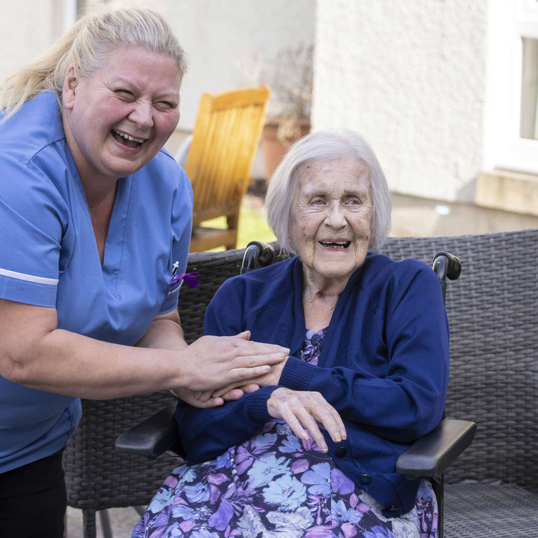 A staff member holds a care home residents hand in the garden 