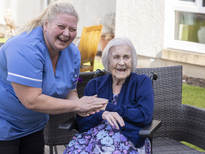 A staff member holds a care home residents hand in the garden 