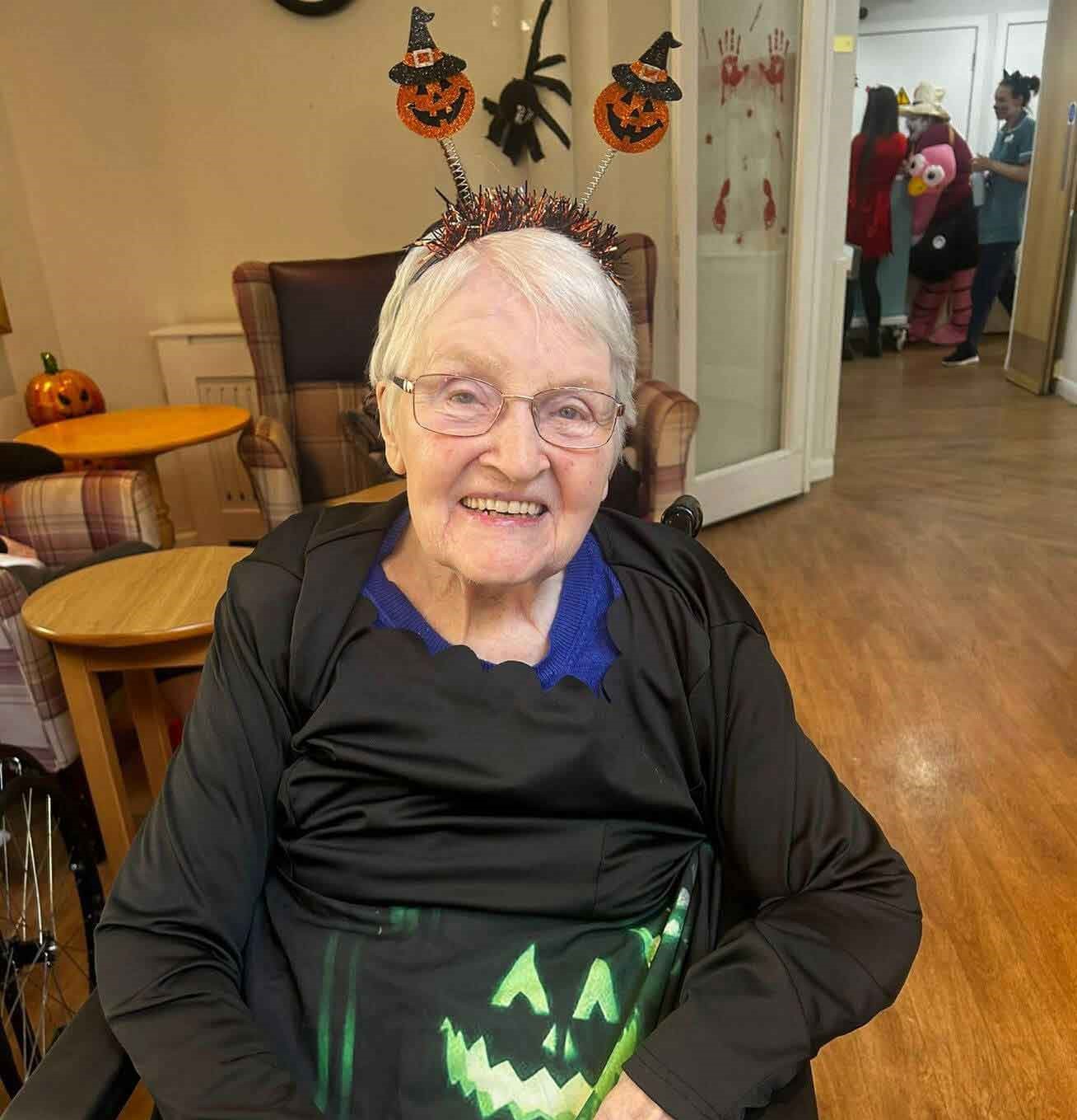 Resident Betty is dressed up and ready for Halloween. She wears a pumpkin headband and ghoulish dress. 