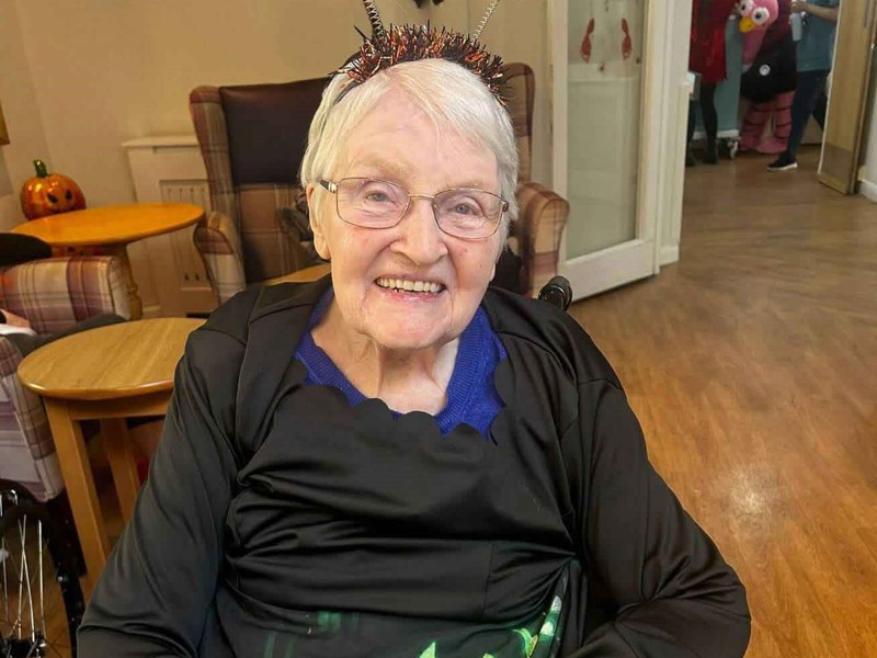 Resident Betty is dressed up and ready for Halloween. She wears a pumpkin headband and ghoulish dress. 