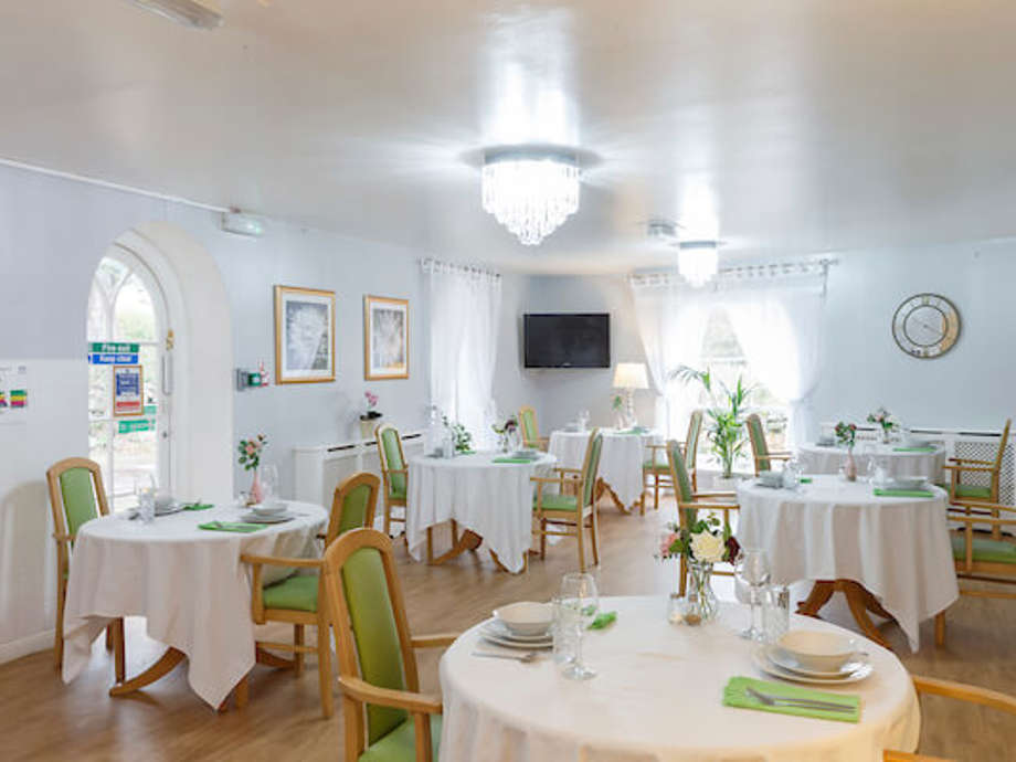 Sunlight floods a spacious dining room with tables and chairs arranged for a meal