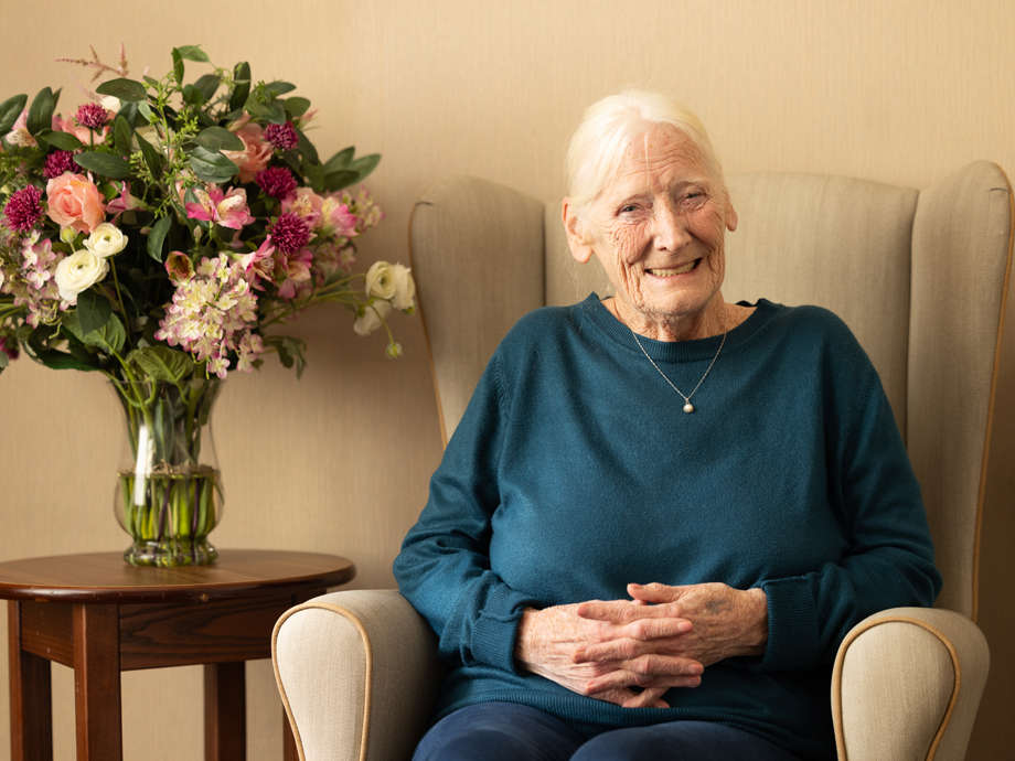 A smiley resident sits beside a table full of flowers