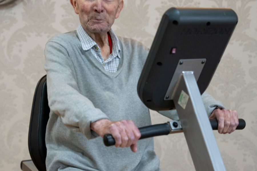 A care home resident is exercising on his indoor bike within the homes activities room