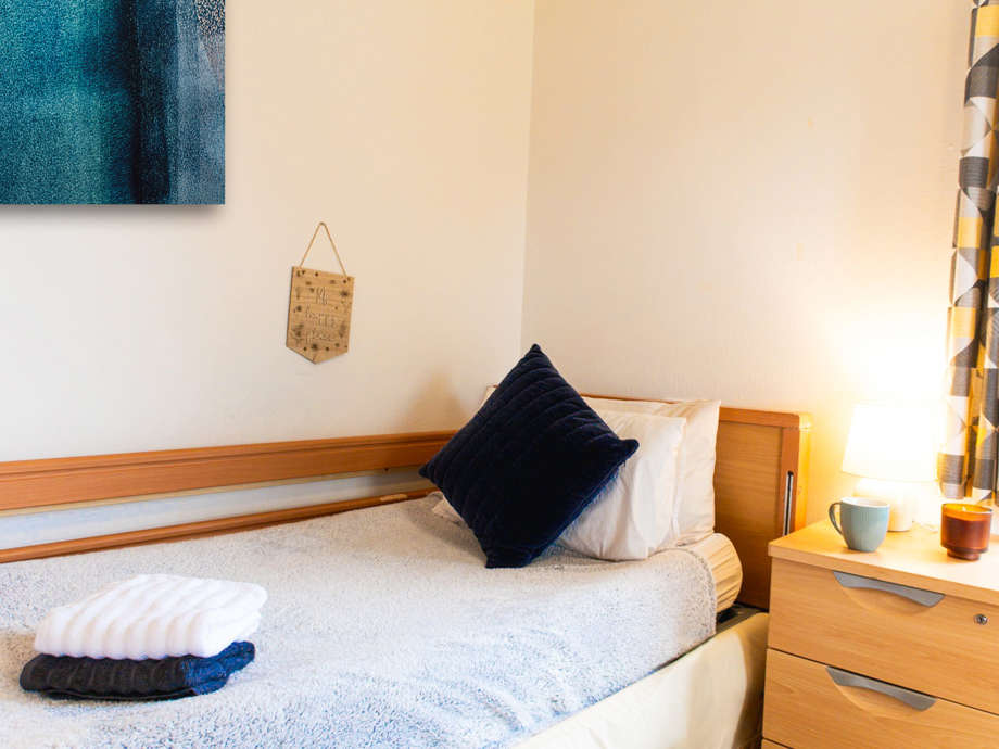 Care home bedroom with a wooden bed and side table. Navy blue accents and artwork personalise the space.