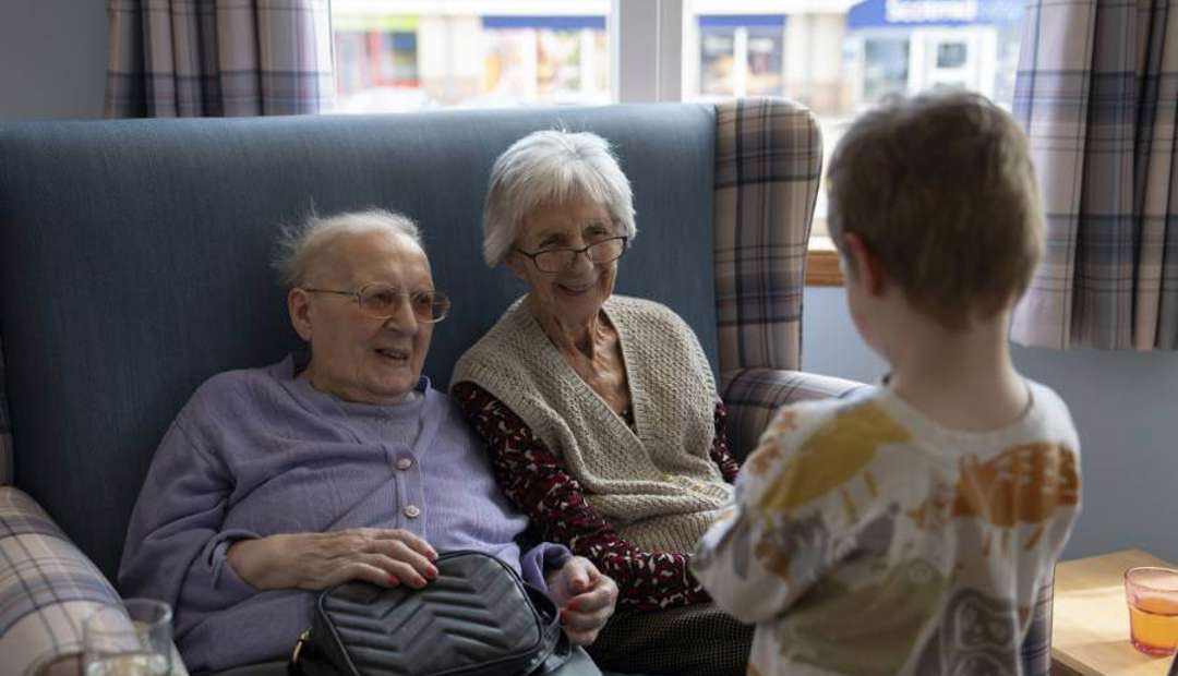 Two care home residents share a warm smile with a visiting nursery child