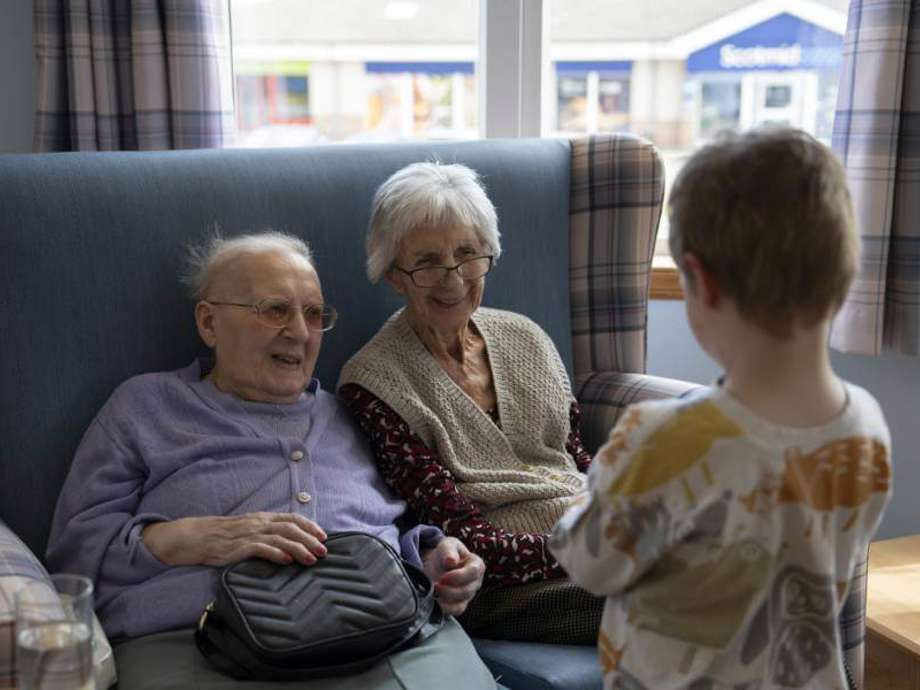 Two care home residents share a warm smile with a visiting nursery child