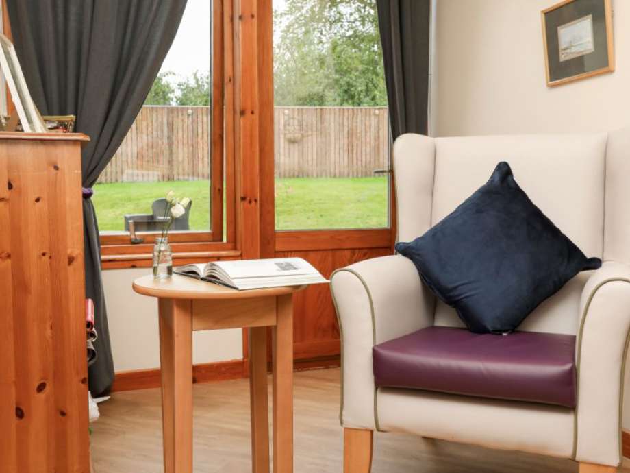 A cosy seating area in a care home. The nook has a chair with a navy blue pillow next to a small table holding an open book.