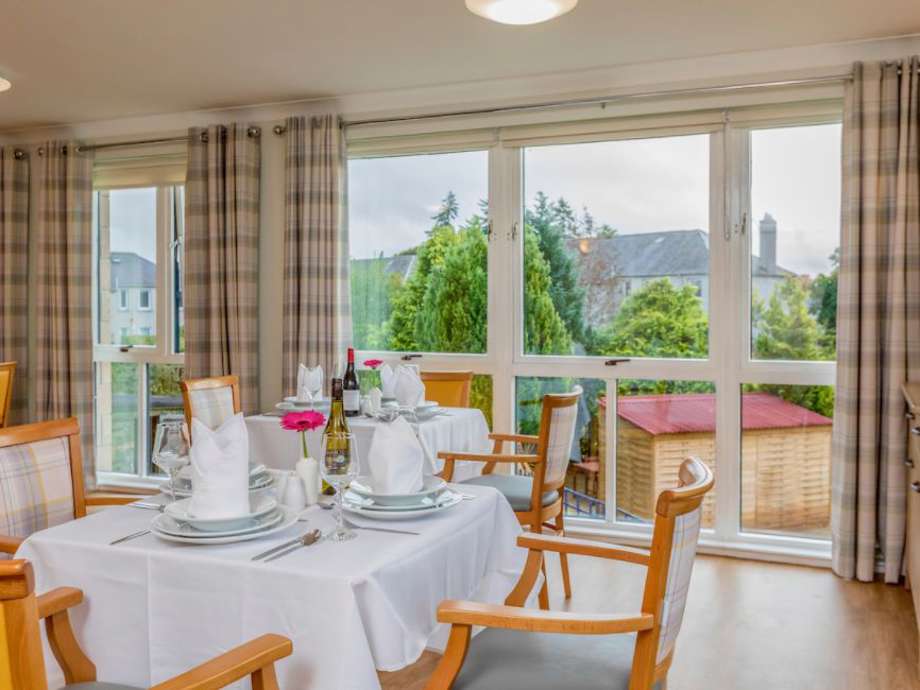 Multiple tables and chairs make up this dining room, with napkins and tableware throughout, and overlooking the garden through large floor to ceiling windows