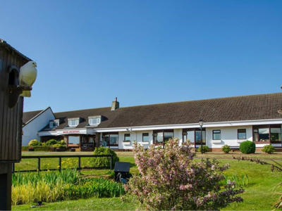 Malin Court Care Home Exterior - a white building with large landscaped gardens and blue skies overhead