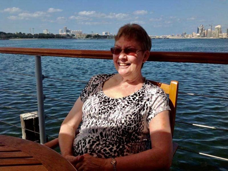 Rosepark resident Grace Ross sits at a wooden furniture set, smiling, with the Dubai sea and skyline as her backdrop 