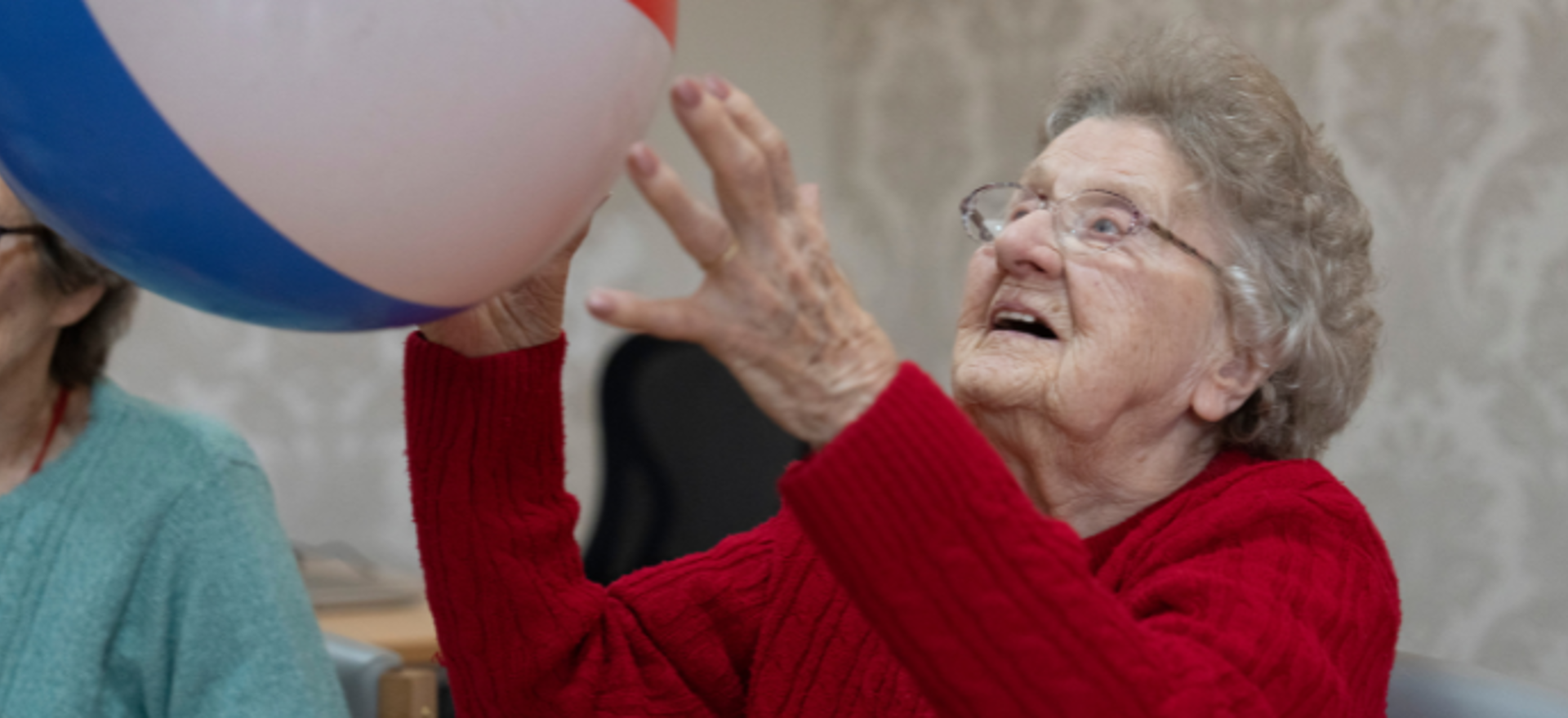 A woman in red knitwear hits a beach ball in an exercise class