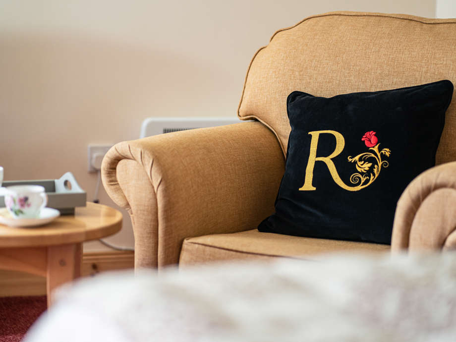 A chair with Renaissance At branded cushion, a golden R with a red rose, next to a table offering tea