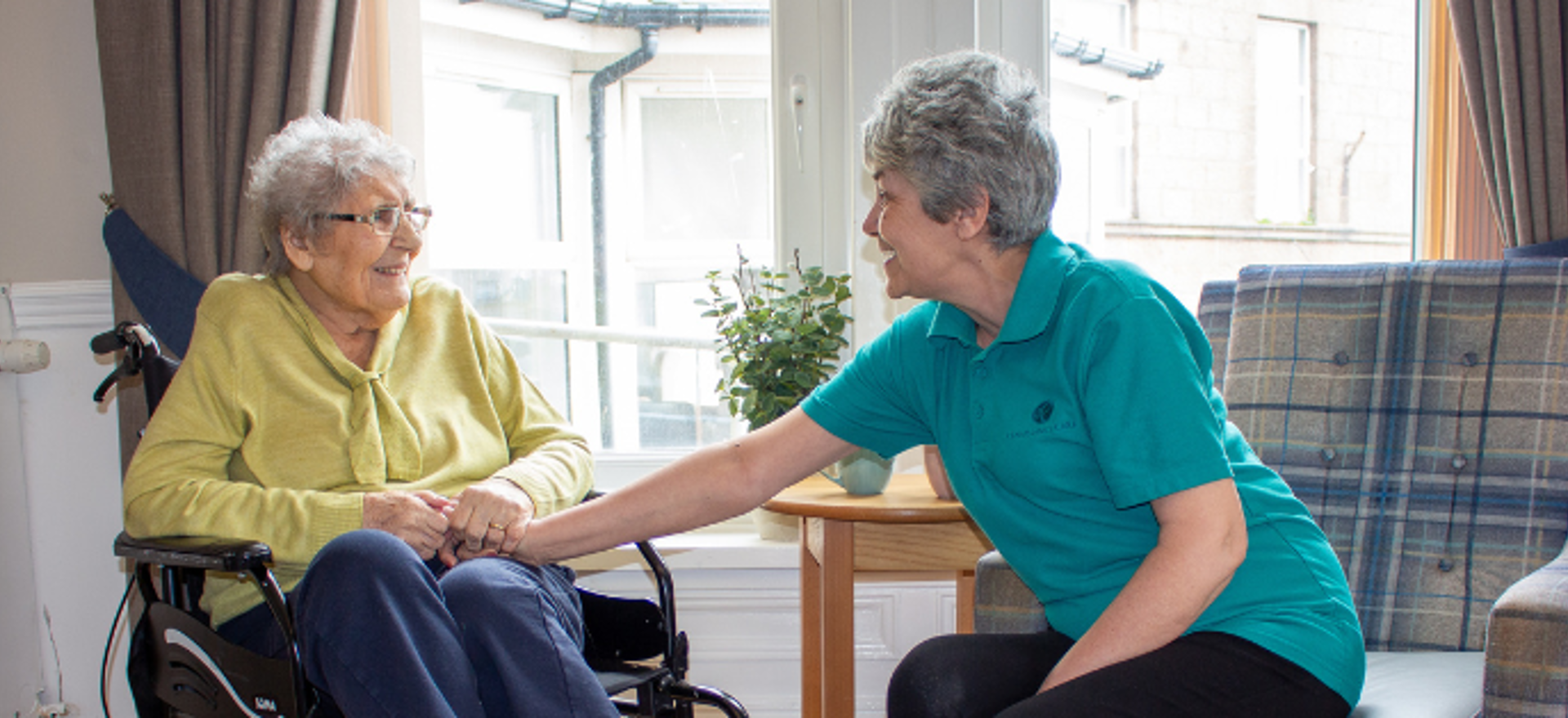 Wyndwell resident and staff member sitting together and smiling within the communal lounge 