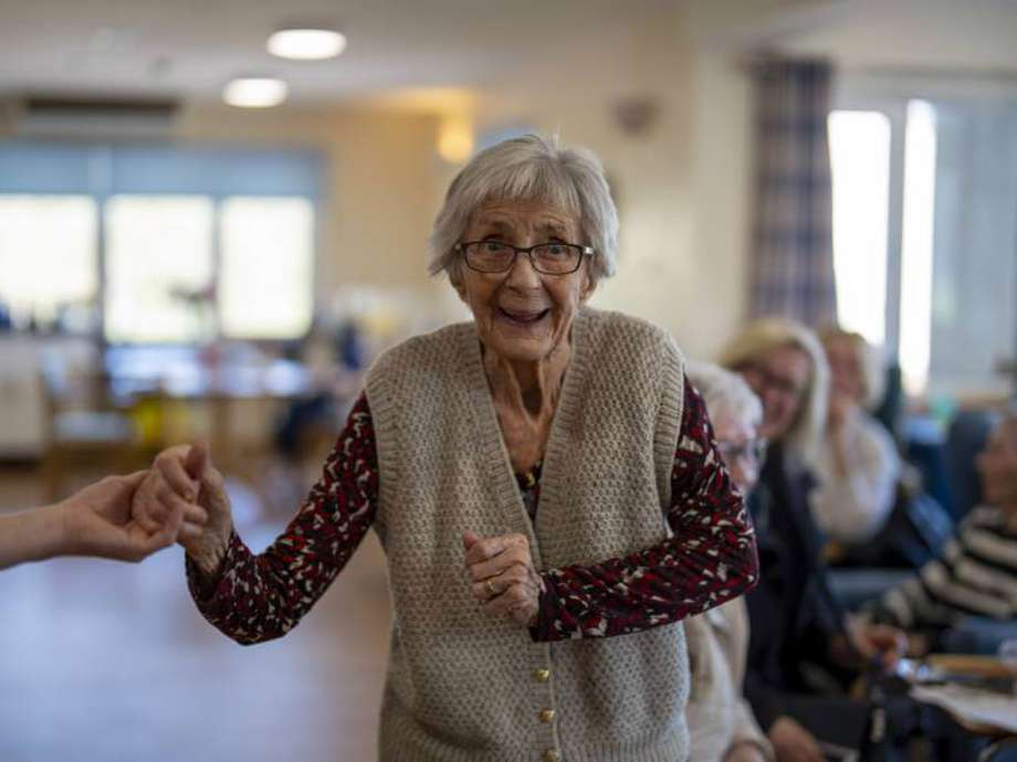 Woman enjoys dancing, holding hands with a care assistant (out of view).