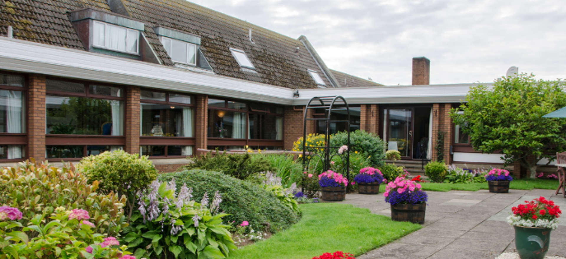 Malin Court exterior, a building with a red/brown brick facade and a vibrant flower garden.