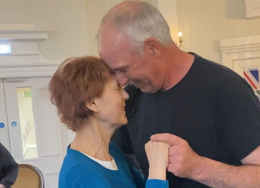 A care home resident and her husband dance together within the homes lounge area