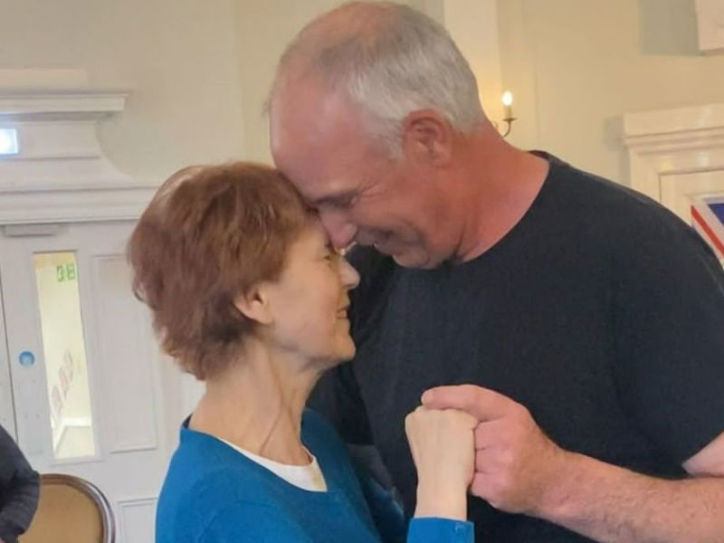 A care home resident and her husband dance together within the homes lounge area