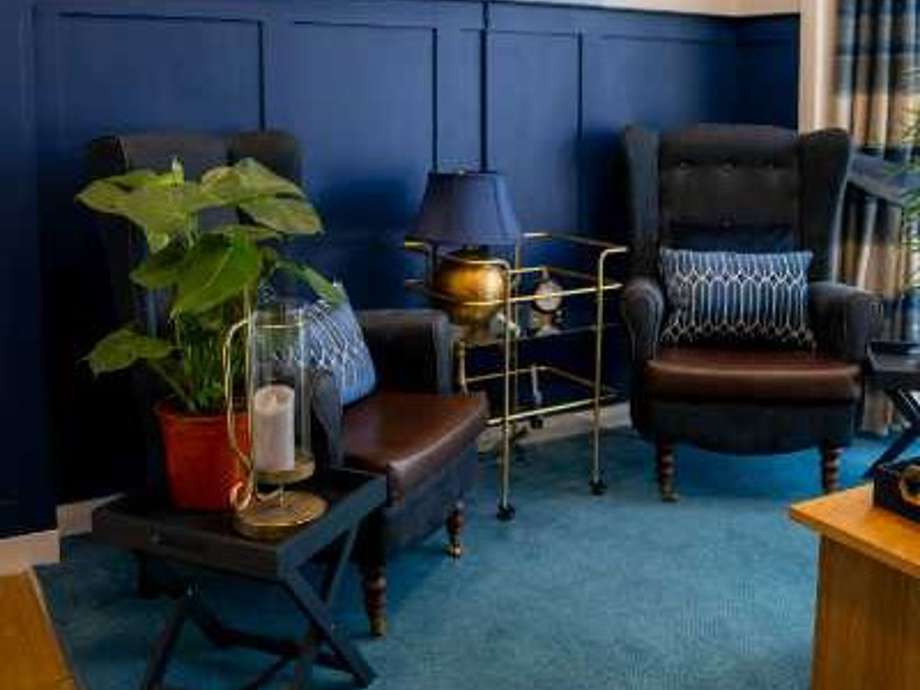 Sophisticated communal lounge featuring high-backed chairs and rich wood paneling. Homey plants and navy accents create a warm and inviting atmosphere