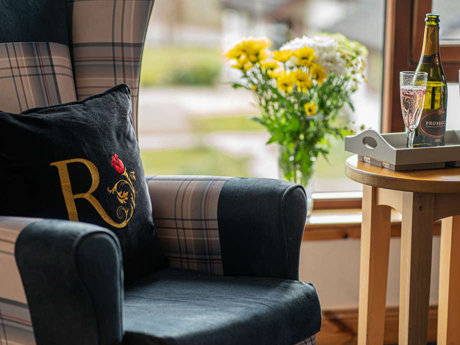 Close-up of a high-backed chair beside a window. Two flutes of prosecco rest on a nearby wooden table